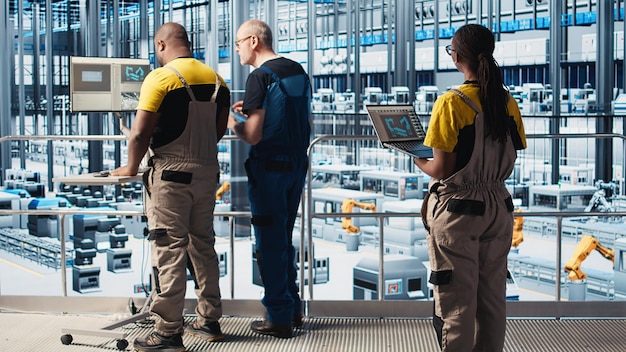 An image depicting a diverse group of engineers and technicians collaborating in a modern US factory setting. They are reviewing data on tablets and large monitors, with advanced machinery visible in the background. The scene emphasizes teamwork, data analysis, and the integration of technology in manufacturing.