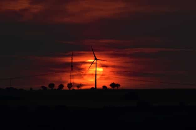 A wind turbine farm silhouetted against a fiery sunset, representing the challenges to renewable energy initiatives.